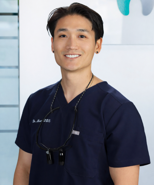 Dr. Sungjun Andy Moon, general dentist in Kelowna, wearing navy scrubs and smiling in a modern dental clinic